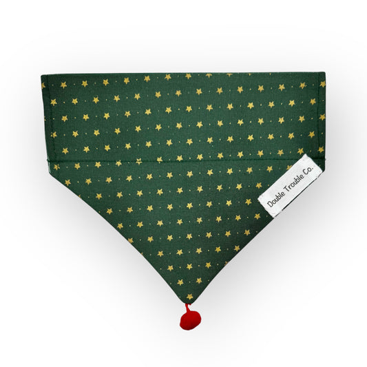 A green over-the-collar bandana with gold stars and a red or white pom pom, with a label showing the brand name 'Double Trouble Co.'.